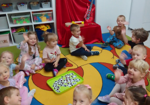Dzieci siedzą na dywanie wokół tacy, na której są odnalezione przez dzieci nutki.