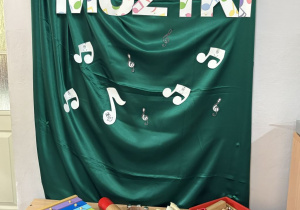 Tablica dekoracyjna z zielonym materiałem oraz napisem Dzień Muzyki i nutkami, a pod dekoracją przedszkolne instrumenty