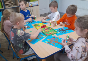 Sześcioro dzieci siedzi przy stole i wykonuje pracę plastyczną "Jesienne drzewo".