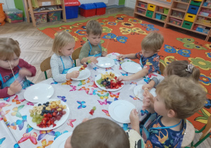 4.Dzieci nawlekają na patyczki owoce.