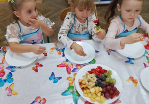 6.Trzy dziewczynki przygotowują szaszłyki z owoców.