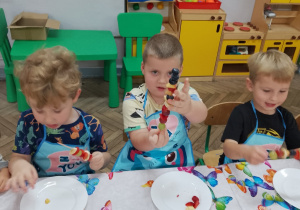 8.Kornel z duma prezentuje zrobiony przez siebie szaszłyk, dwaj koledzy jeszcze pracują.