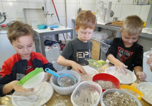 Bartek, Bruno i Wiktor bawią się mąką i ziarnami zbóż przy stole.