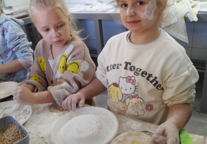 Nadia wykonała na talerzu babeczkę z mąki. Obok stoi Tosia i ogląda dzieło koleżanki.