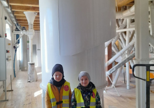 Dwóch chłopców stoi obok siebie podczas zwiedzania młyna. Za nimi znajduje się duży wentylator.