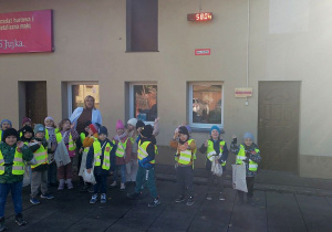 Dzieci razem z Panią właścicielką stoją na dużej wadze przed budynkiem młyna.