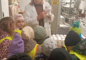 Pani pokazuje dzieciom mąkę w torebce. W tle maszyna do pakowania mąki.