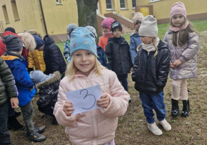 Nadia trzyma w dłoniach białą kopertę z cyfrą 3.