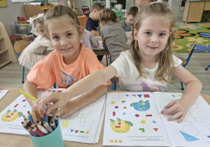 13.Oliwia i Ola siedzą przy stoliku i kolorują pajacyka z figur geometrycznych