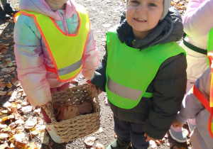 Nikodem i Laura trzymają koszyk, do którego dzieci wrzucają jesienne dary.
