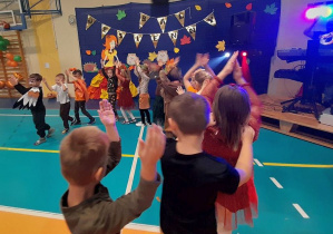 Dzieci jadą w pociągu przy muzyce. W tle dekoracja z napisem Bal Jesienny.