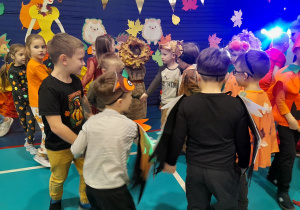 Dzieci tańczą w małych kółkach. W tle fragment jesiennej dekoracji.