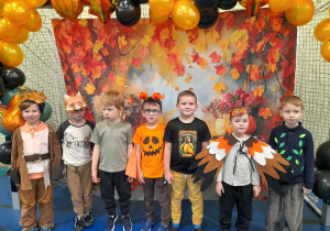 Grupka chłopców pozuje do wspólnego zdjęcia. W tle baner z motywem jesiennym i balonowa girlanda.