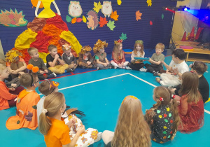 Dzieci siedzą w kole i podają sobie kółko w rytm muzyki.