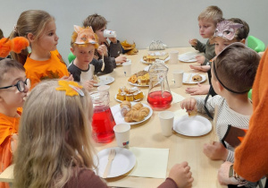 Grupka dzieci siedzi przy stoliku podczas słodkiego poczęstunku.