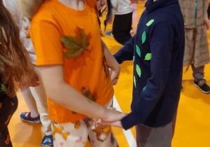 Marysia i Adam tańczą w kółeczku przy muzyce trzymając się za ręce. W tle inni uczestnicy balu.