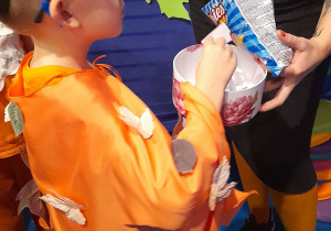 Mikołaj stoi przed Panią i losuje zagadkę z pojemnika.