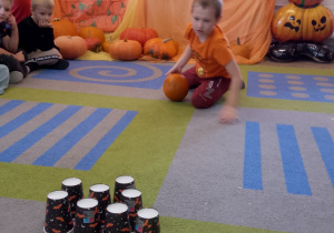 Antek stoi trzymając dynię, przed nim stoją papierowe kubeczki.