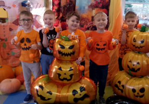 Grupka chłopców pozuje do zdjęcia na tle dekoracji z okazji Dnia Dyni z dyniowymi balonami i otrzymanymi upominkami.