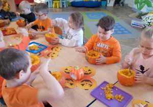 Grupka dzieci wydrąża dynie.