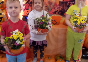 Trójka dzieci prezentuje wykonane dyniowe kompozycje.