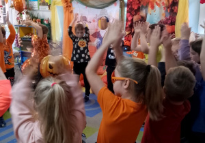 Dzieci stoją w kole i klaszczą nad głowami, na środku koła stoi dyniowy balon.