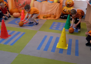 Dwóch chłopców toczy dynie między pachołkami.