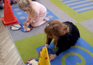 Dwie dziewczynki nakładają na talerzyki pestki dyni.