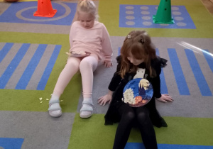 Dwie dziewczynki przenoszą pestki dyni na talerzykach.