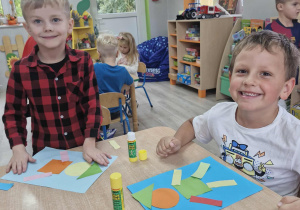 Olek i Franek siedzą przy stoliku i wyklejają pajacyka z figur geometrycznych.