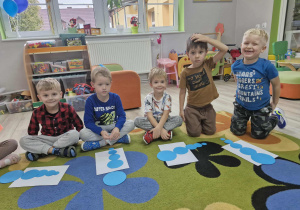 Przedszkolaki siedzą na dywanie i układają niebieskie koła od najmniejszego do największego.