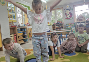 Weronika stoi w okręgu z rozłożonymi rączkami. Przed dziewczynką leży kostka z wyrzuconymi czterema kropkami.