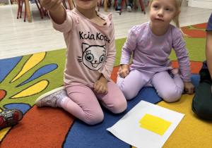 Dziewczynka podnosi wycięty żółty kwadrat.