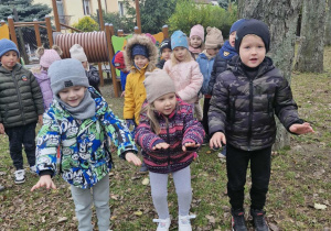 Oluś, Maja i Julek stoją w ogrodzie przedszkolnym i trzymają rączki wyciągnięte przed sobą.