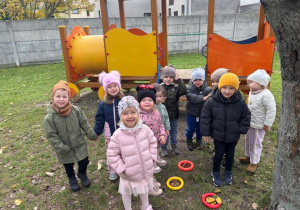 Dzieci pozują do zdjęcia przy obręczach, w których są liście, kasztany oraz orzechy włoskie.