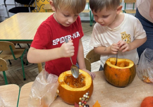Chłopcy stojąc przy stoliczkach wydrążają środek dyni