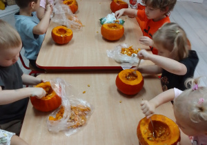 Pszczółki przy długim stole usuwają łyżkami nasiona z dyni.