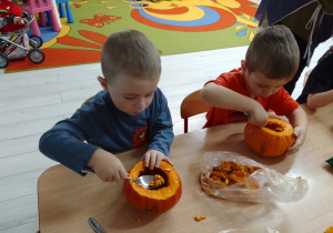 Michał i Olaf usuwają łyżkami nasiona ze środka dyni.