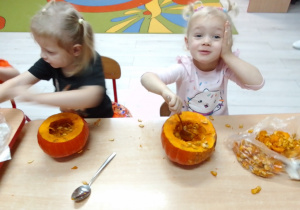 Maja i Kornelia przy stole wyjmują łyżkami nasiona z dyni.