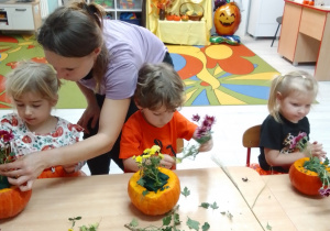 Pani Kasia pomaga Emilce ułożyć kwiaty w dyniowej doniczce, obok Michał i Maja.