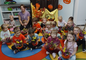 Maluchy i Pani Kasia pozują do zdjęcia prezentując swoje dyniowe kompozycje. Z tyłu dekoracja na Dzień Dyni.