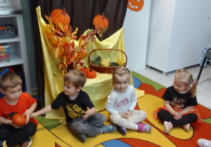Dzieci na dywanie podczas zabawy z dynią. W tle dekoracja i napis Dzień Dyni.