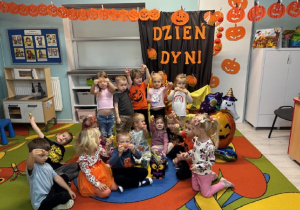 Dzieci trzymają w rączkach cukierki i pozują na tle dekoracji . Na dywanie stoi torebka z filcu w kształcie sowy a w środku znajdują się lizaki dla dzieci.