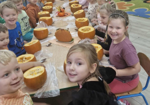 Dzieci siedzą przy długim stole, na którym widać rozłożone dynie
