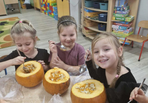 Trzy dziewczynki wydrążają dynie łyżkami