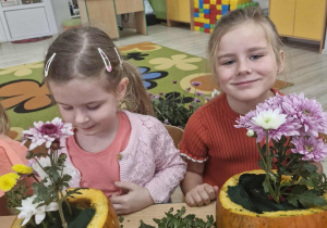 Ola i Weronika umieszczają kwiaty w dyniowych doniczkach