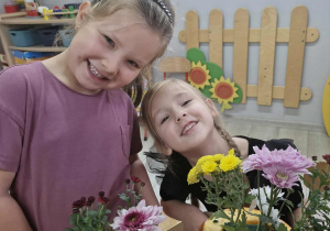 Maja i Zuzia uśmiechają się podczas umieszczania jesiennych kwiatów w doniczkach z dyni