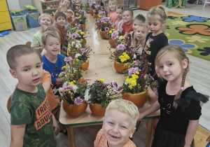 Dzieci siedząc przy stole cieszą się z efektów swoich prac