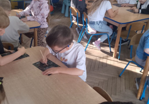 Dzieci siedzą przy stolikach i wydrapują kolorowe bajeczki.