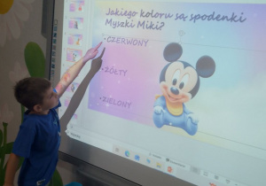 Mikołaj na tablicy interaktywnej wskazuje prawidłową odpowiedź quizu nt. bajek.